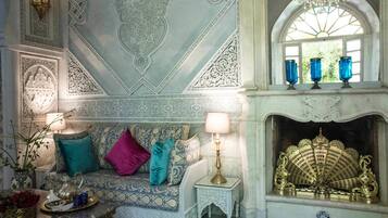 A room with a patterned sofa, a small table with a lamp, and a decorative fireplace.