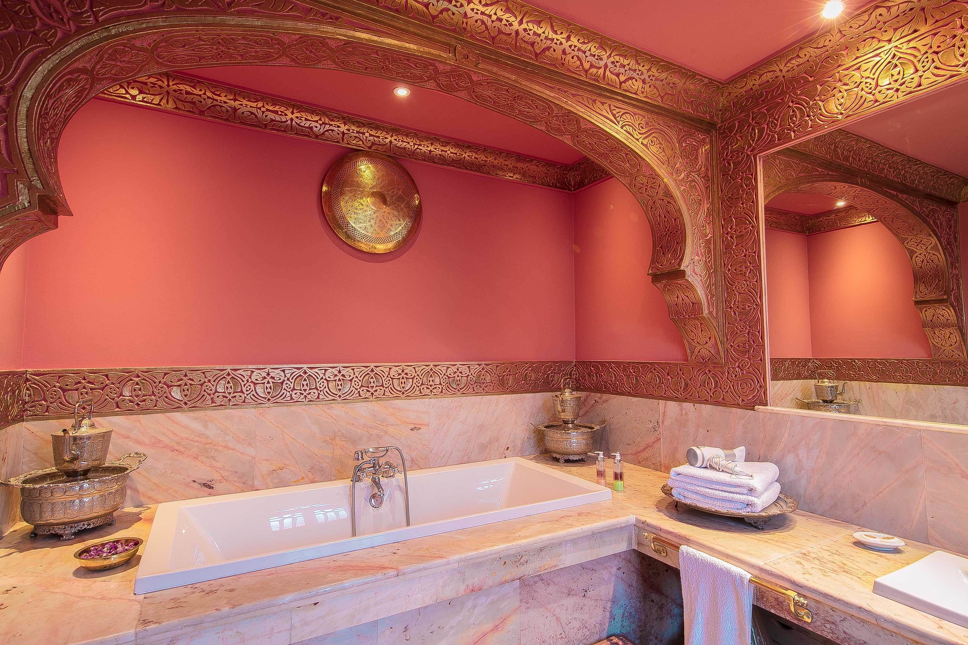A luxurious bathroom with a large white bathtub, ornate gold detailing on the walls and ceiling, and a marble countertop.
