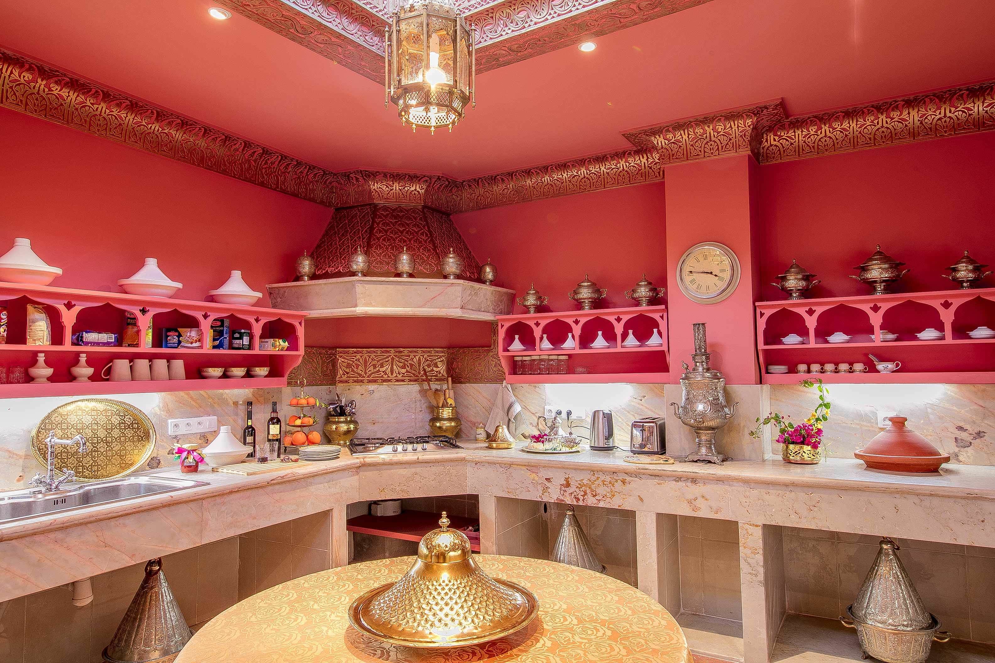 A kitchen with red walls, ornate shelves, and a variety of kitchenware.