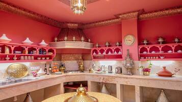 A kitchen with red walls, ornate shelves, and a variety of kitchenware.