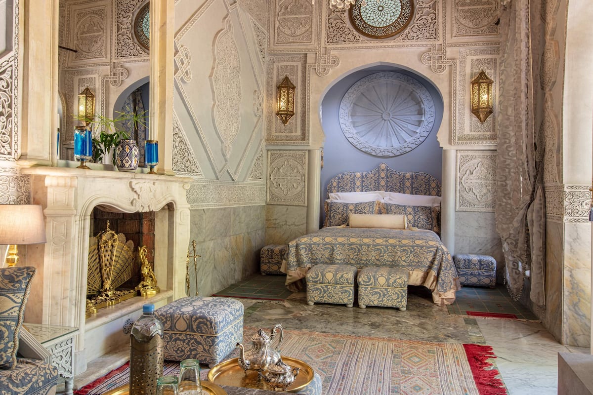 A luxurious room with intricate wall designs, a large bed with patterned bedding, a fireplace, and ornate furniture.