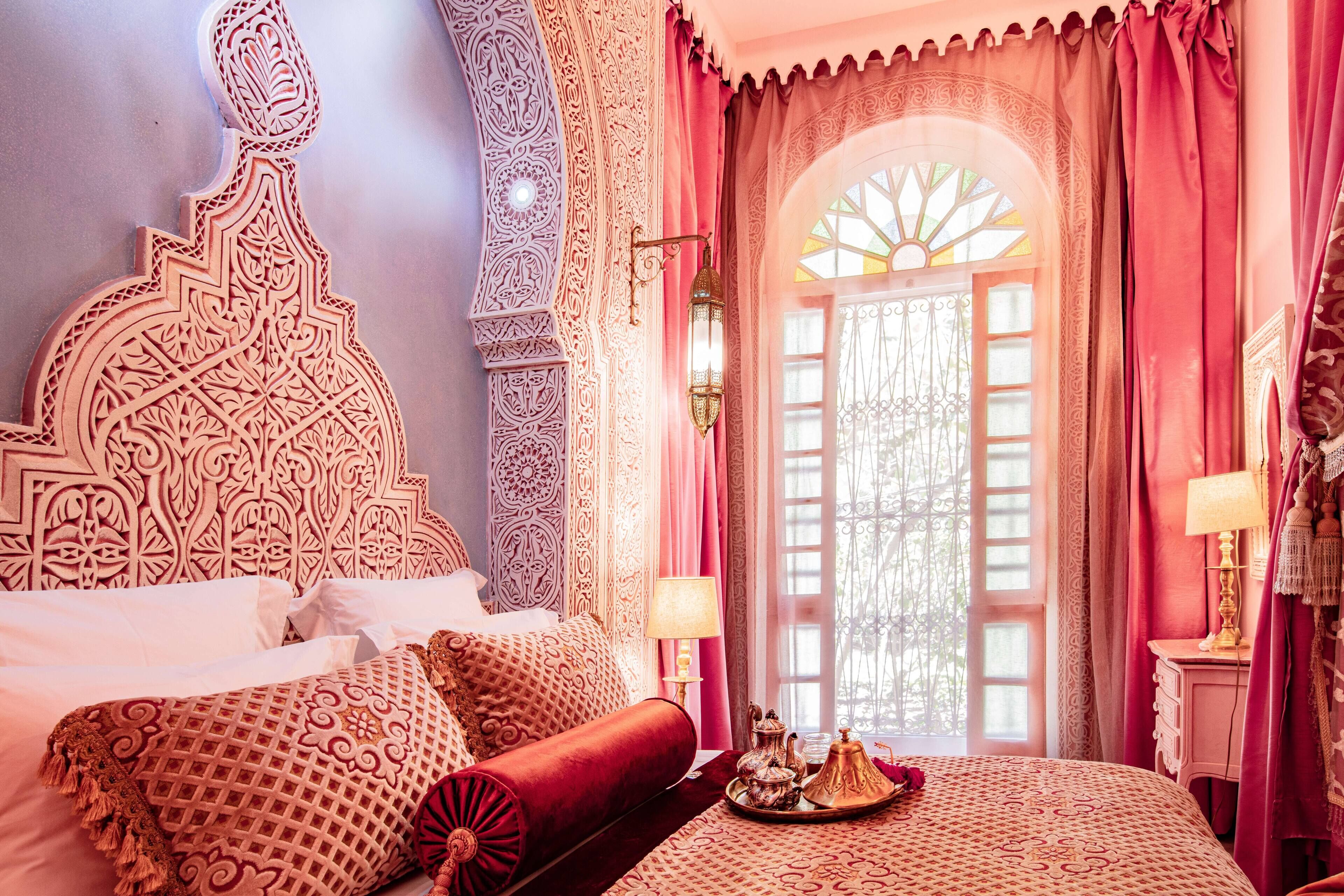 A room with a large, intricately carved headboard, a bed with patterned bedding, and a decorative tray on the nightstand.