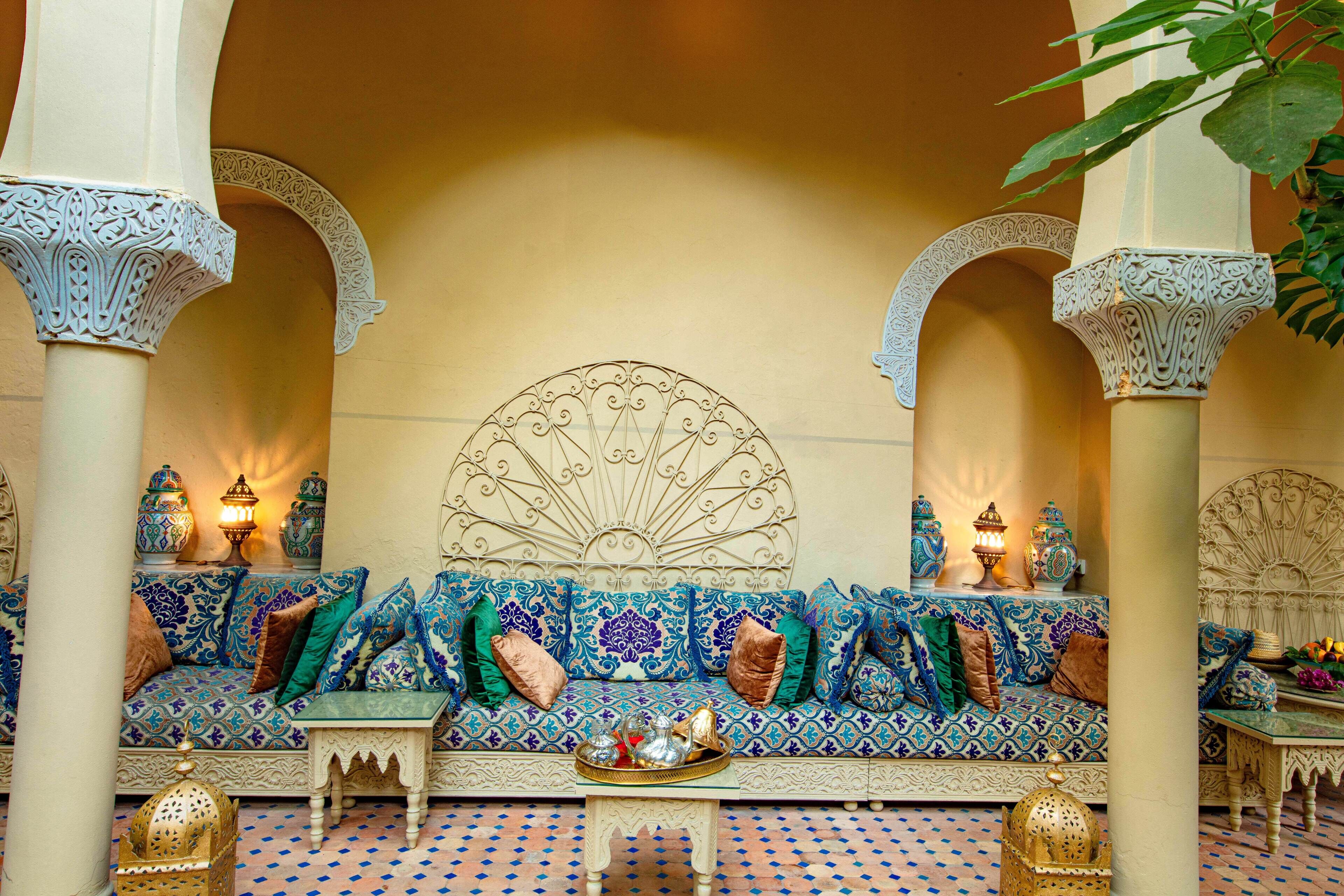 A traditional Moroccan interior with a patterned sofa set, ornate columns, and decorative lamps.