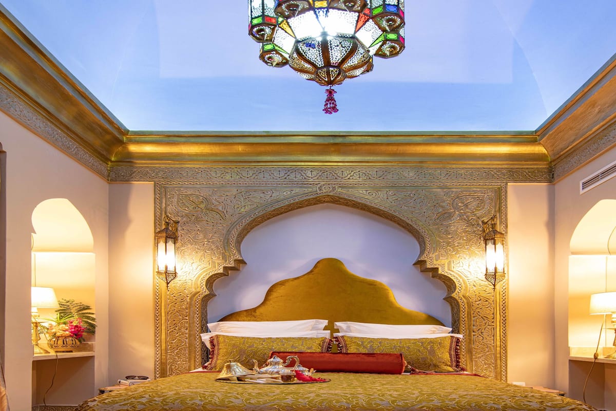 A luxurious bedroom with a large bed, ornate ceiling, and decorative lighting.