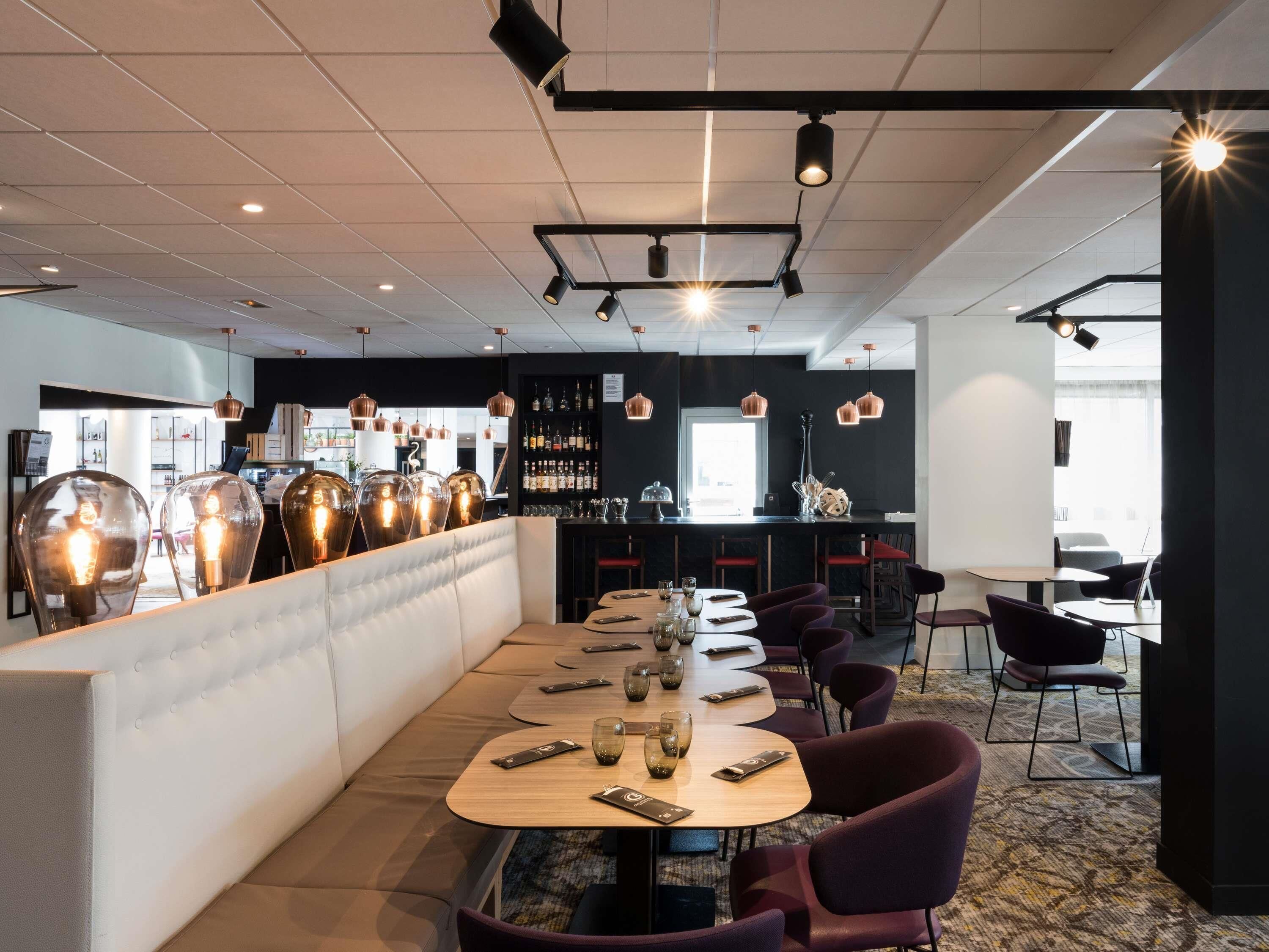 A modern restaurant with a long counter, multiple tables, and a bar area.