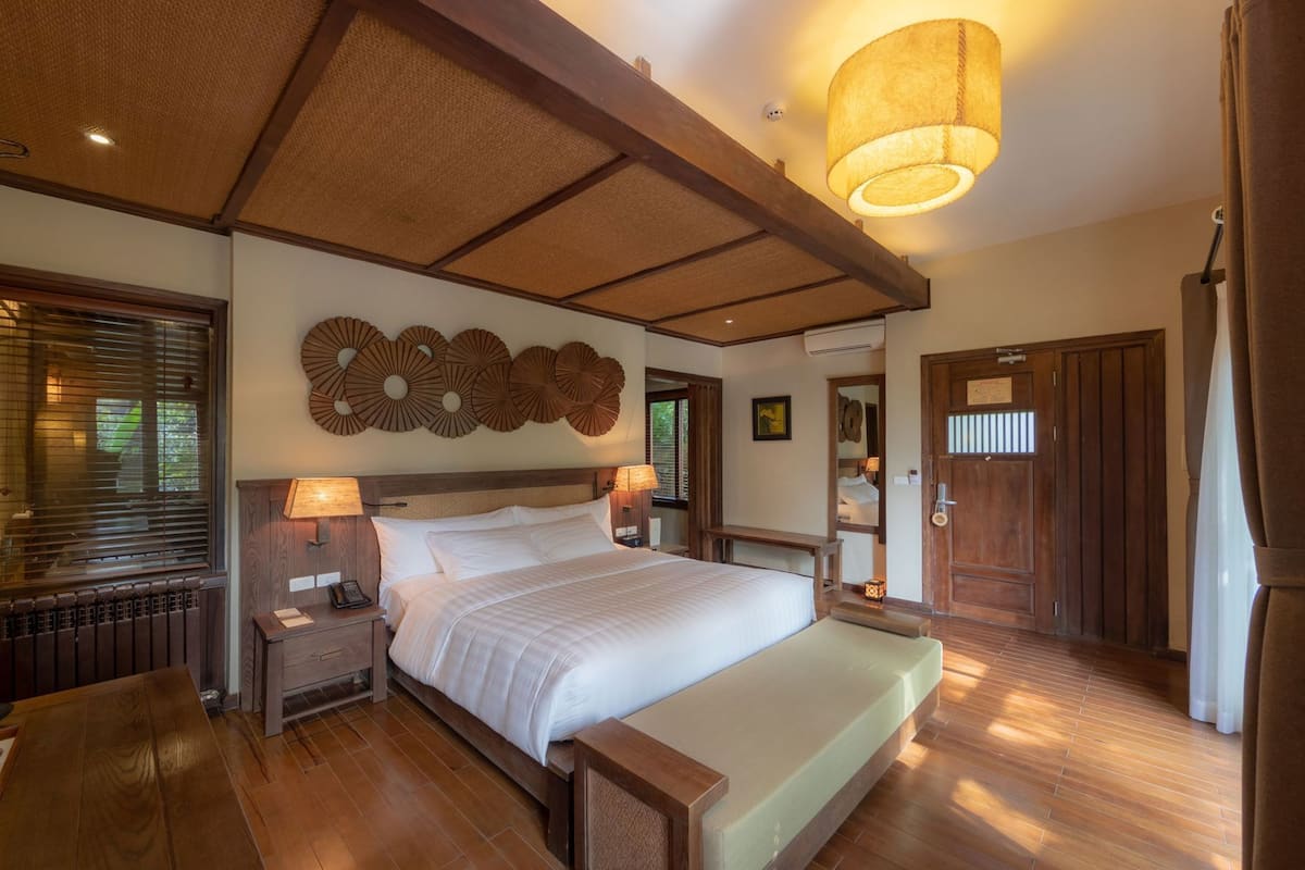 Une chambre spacieuse avec un grand lit, une tête de lit en bois et un ventilateur de plafond.