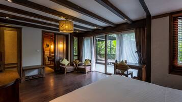 A spacious bedroom with a large bed, wooden flooring, and a view of the outdoors through large windows.