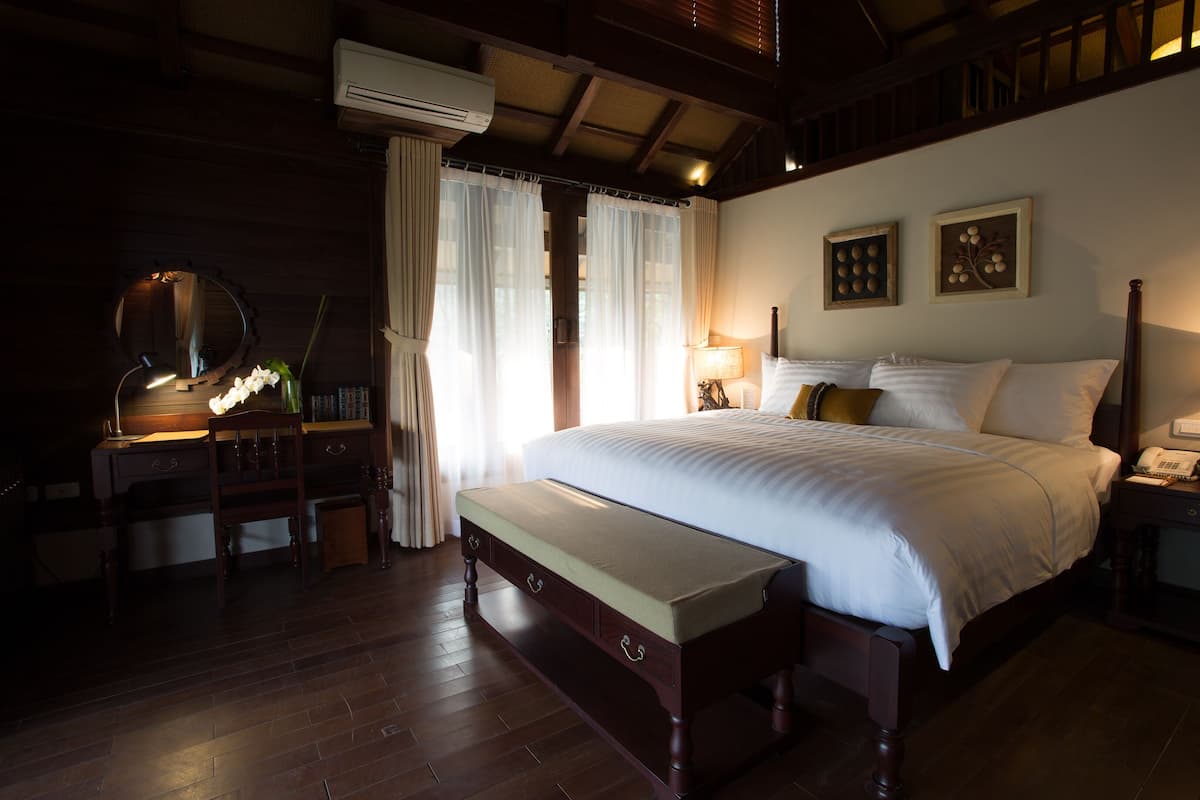 Une chambre à coucher avec un lit en bois, une table de chevet avec une lampe, un miroir, un bureau avec une chaise et un banc.
