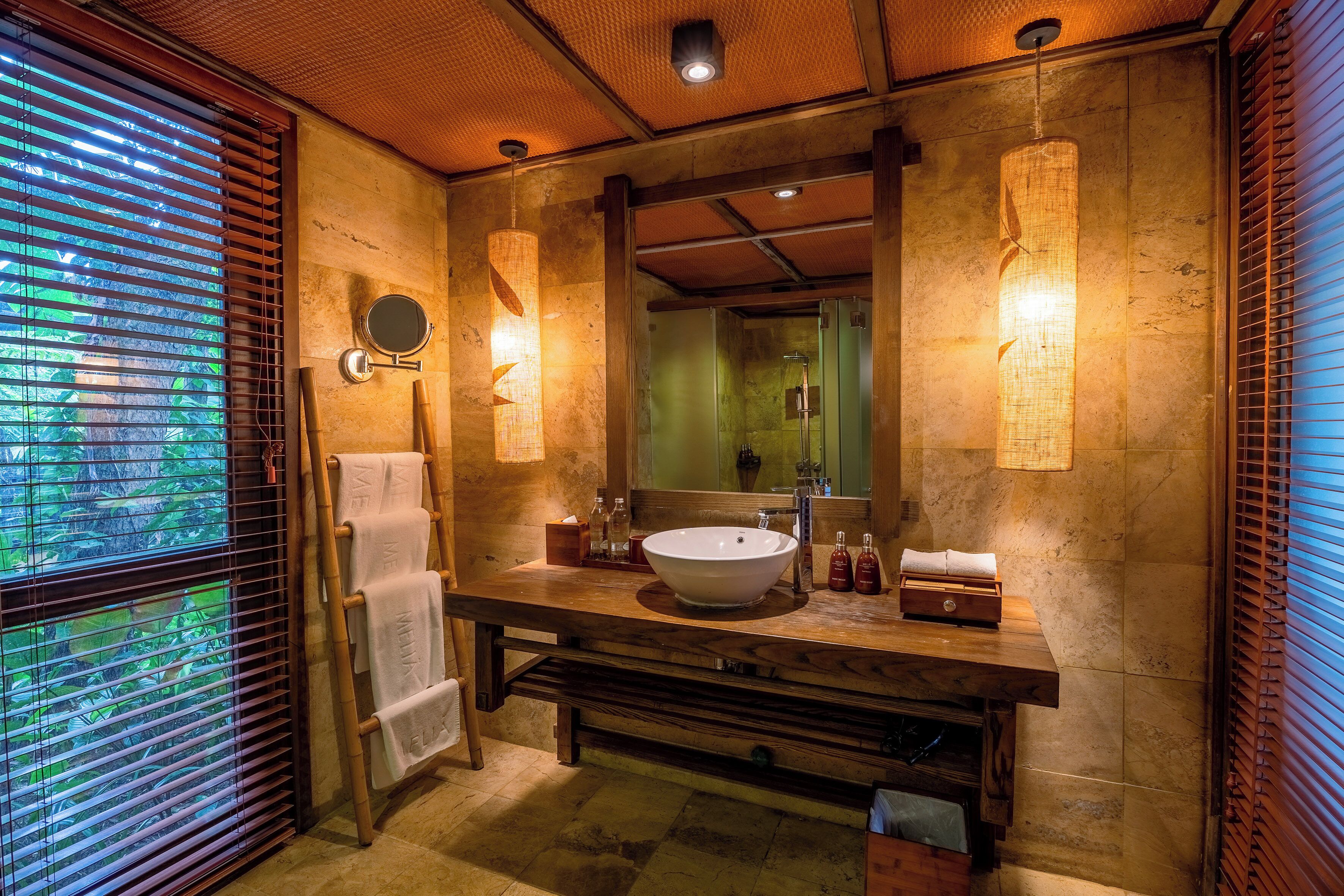Une salle de bain avec un grand lavabo, un meuble-lavabo en bois et un miroir. Des serviettes sont suspendues sur un porte-serviettes et il y a un sèche-serviettes.