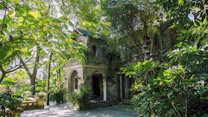 A historic building with a stone facade, arched windows, and a balcony overlooking a garden.