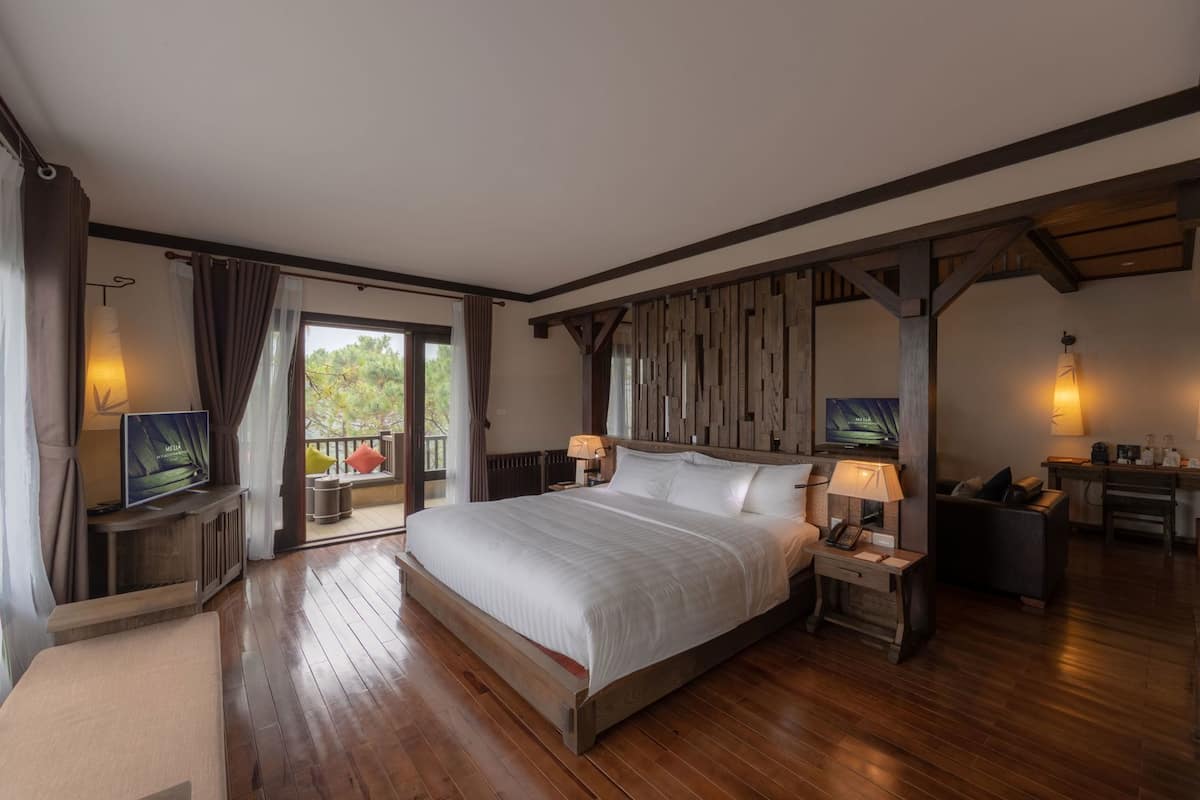 Une chambre spacieuse avec un grand lit, une télévision, un bureau avec une chaise et un balcon avec vue.