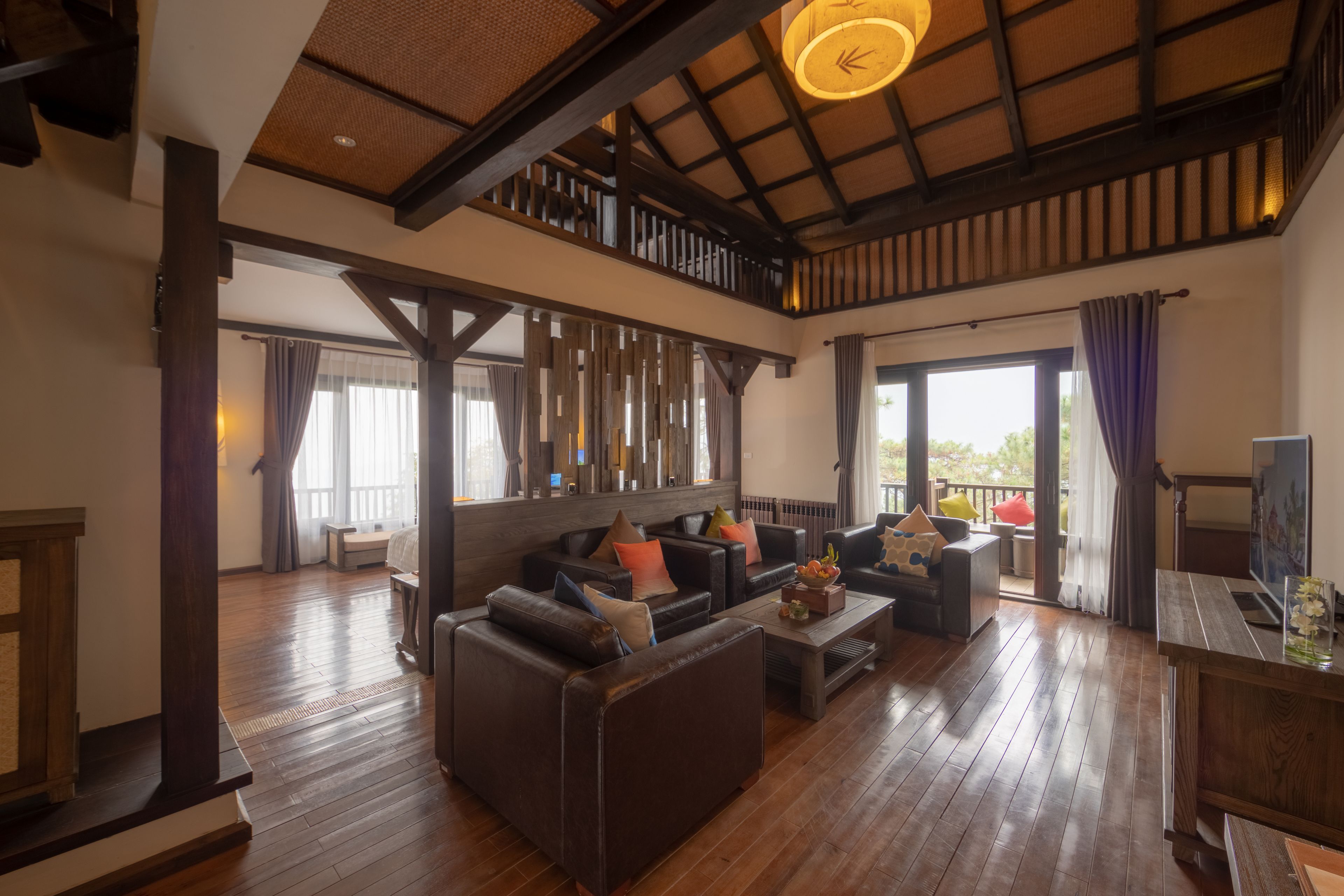 A spacious living area with a high ceiling, wooden flooring, and a seating arrangement including sofas and a coffee table.