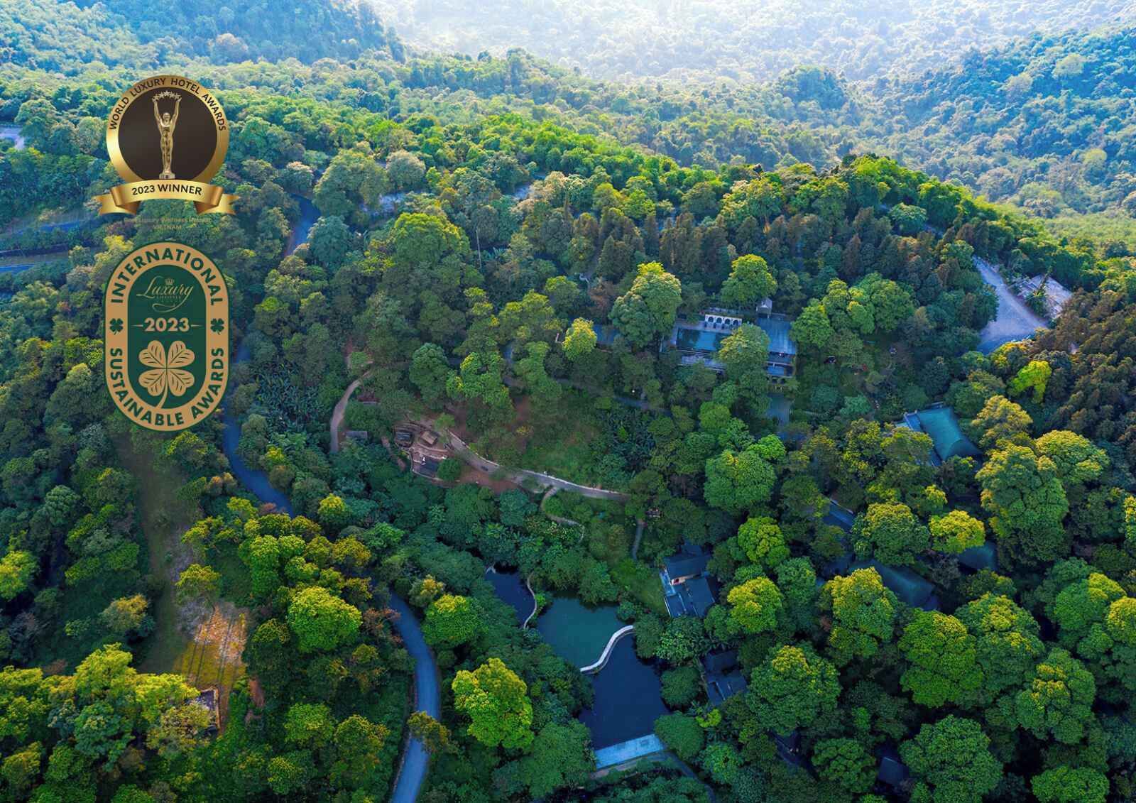 An aerial view of a luxury hotel surrounded by dense forest, with visible pathways and a small water body.