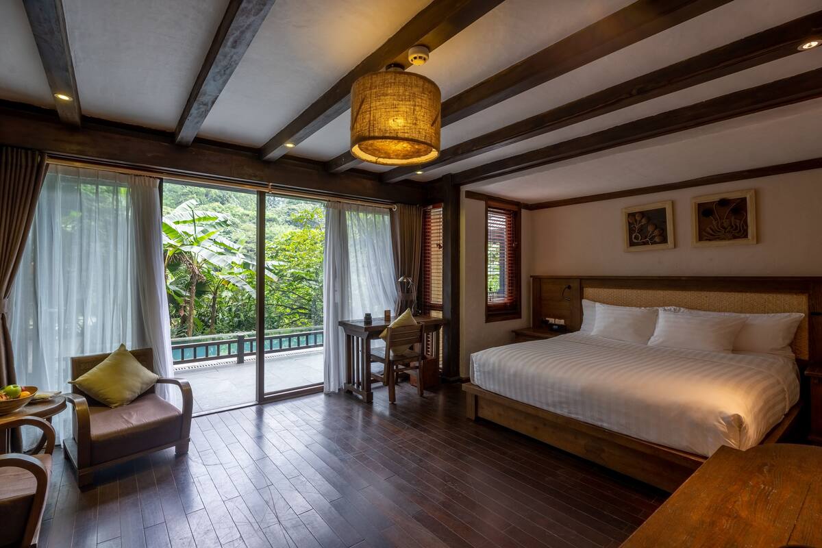 Une chambre dotée d’un grand lit, de meubles en bois, d’un bureau et offrant une vue sur une végétation luxuriante.