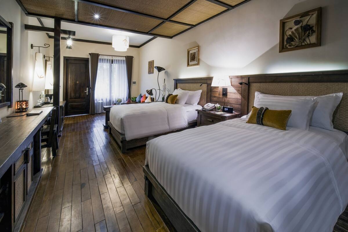 Une chambre d’hôtel avec deux lits, un bureau, une chaise, une lampe et une table de chevet.