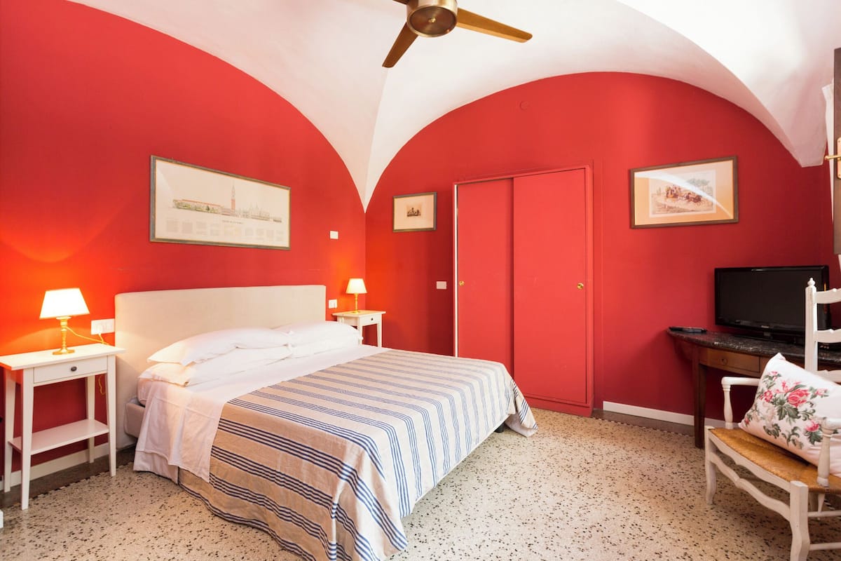 Een slaapkamer met een bed, twee nachtkastjes met lampen, een televisie, een stoel en twee ingelijste foto's aan de muur.