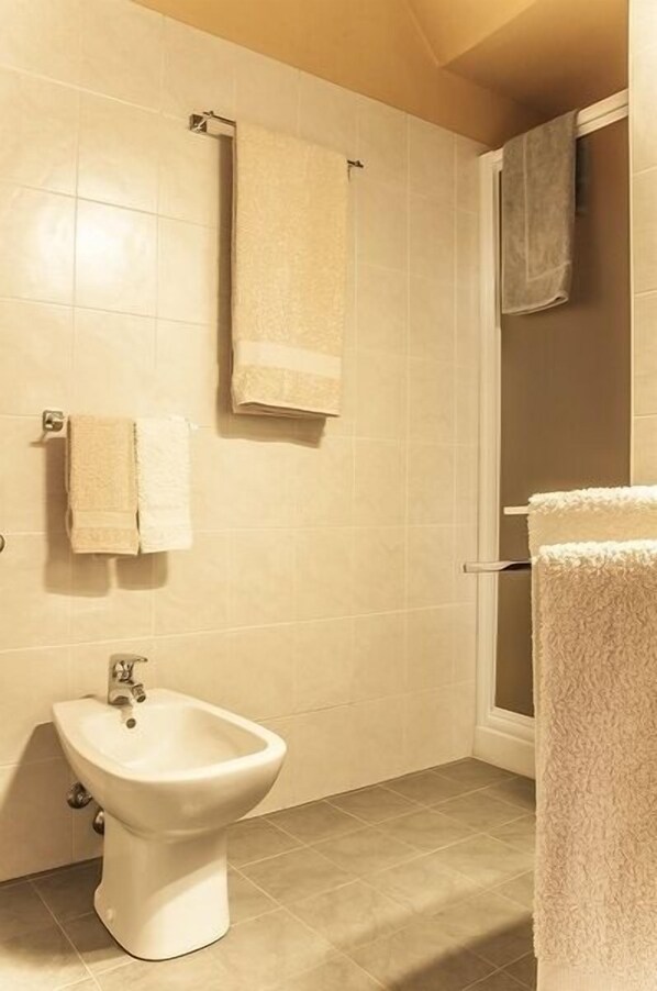A bathroom with beige tiles, a bidet, and two towels hanging on the wall. - B&B Corte delle Muse (San Felice del Benaco)
