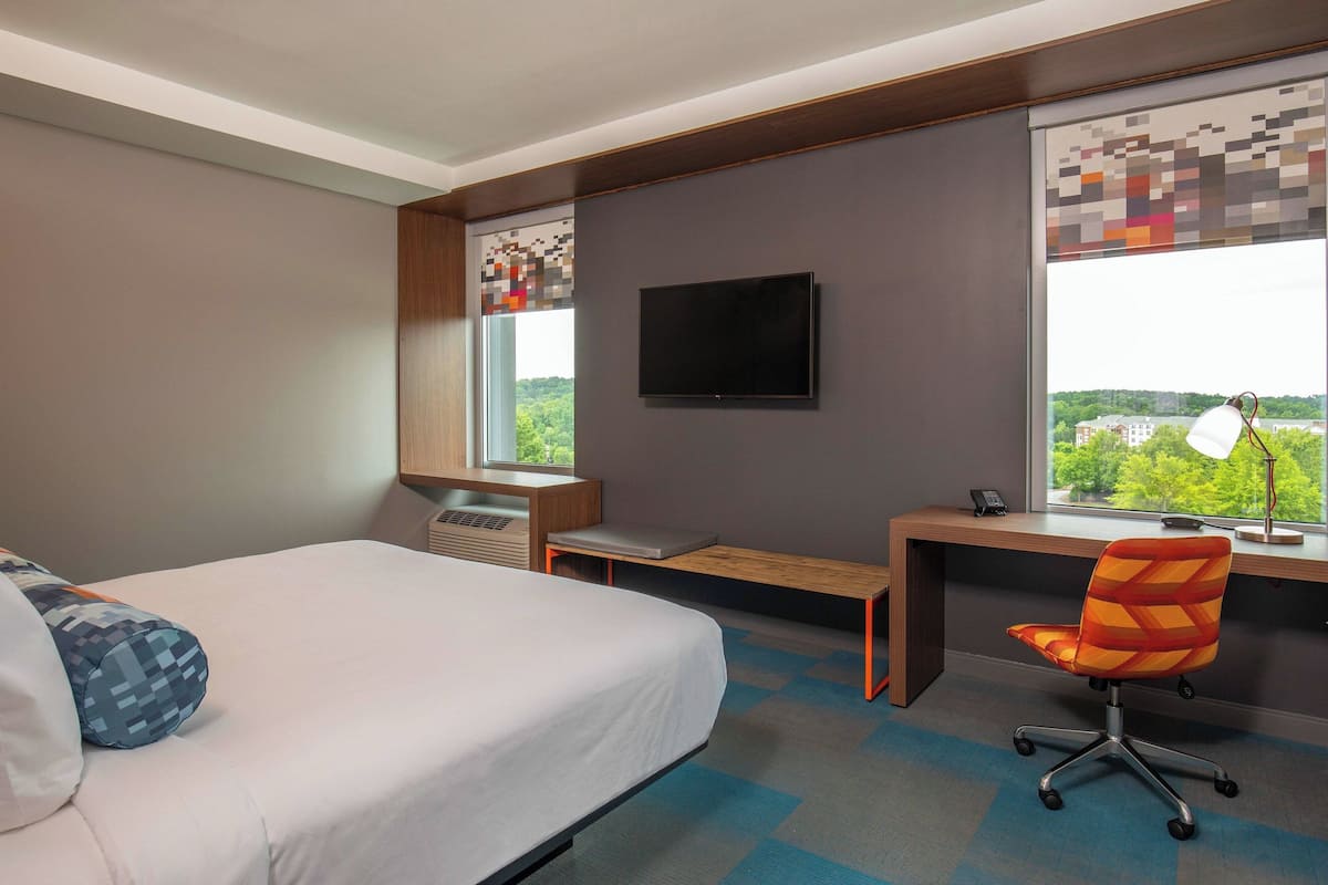Quarto de hotel com cama, escrivaninha, cadeira, televisão e janela com vista.