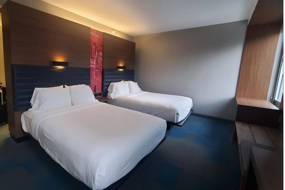 Quarto de hotel com duas camas, uma janela grande e design moderno.