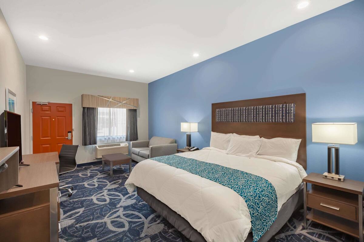 A hotel room with a large bed, a desk, a chair, a TV, and a window with curtains.