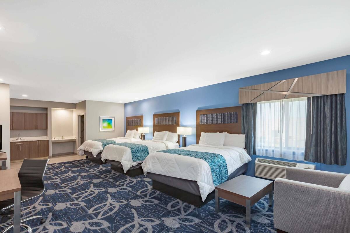 A hotel room with two beds, a desk, a chair, and a large window with curtains.