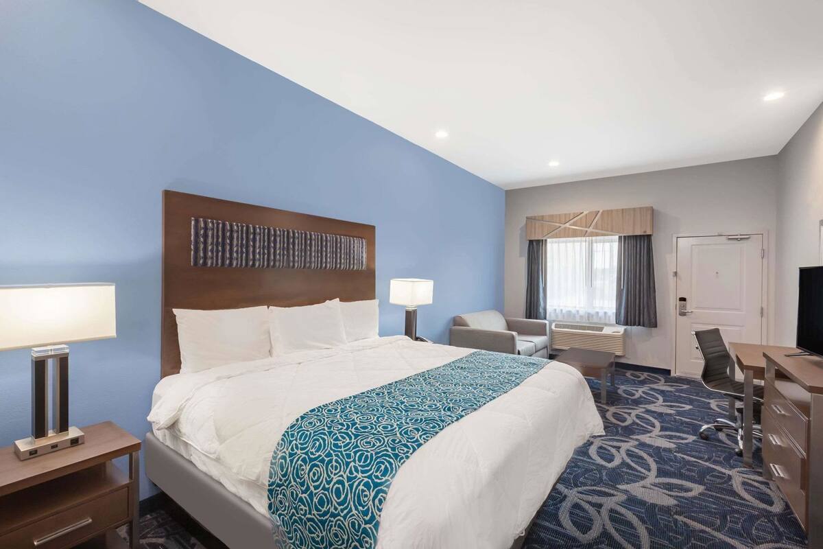 A hotel room with a bed, bedside tables, a desk, a chair, a TV, and a door.