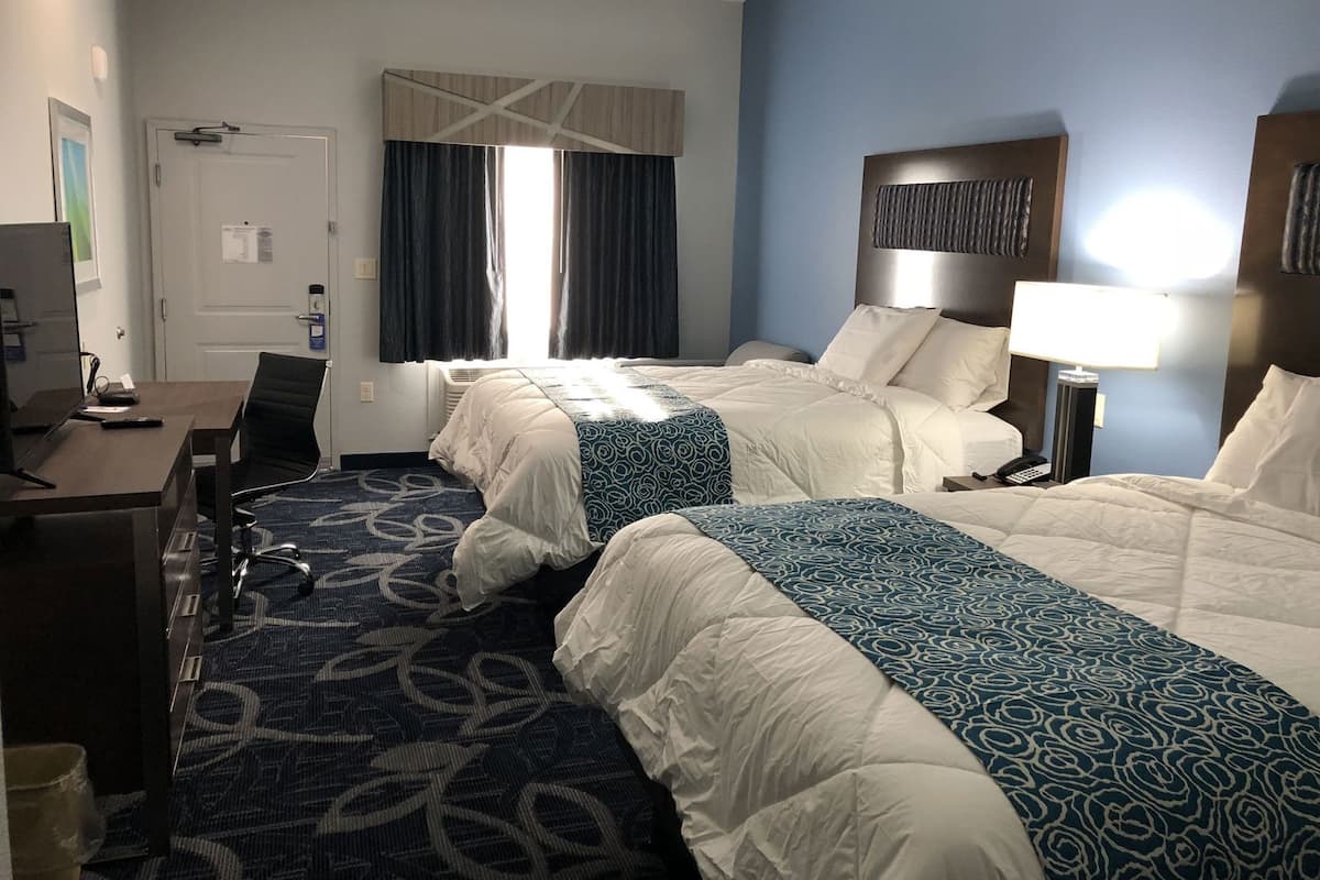 A hotel room with two beds, a desk, a chair, a lamp, and a window with curtains.
