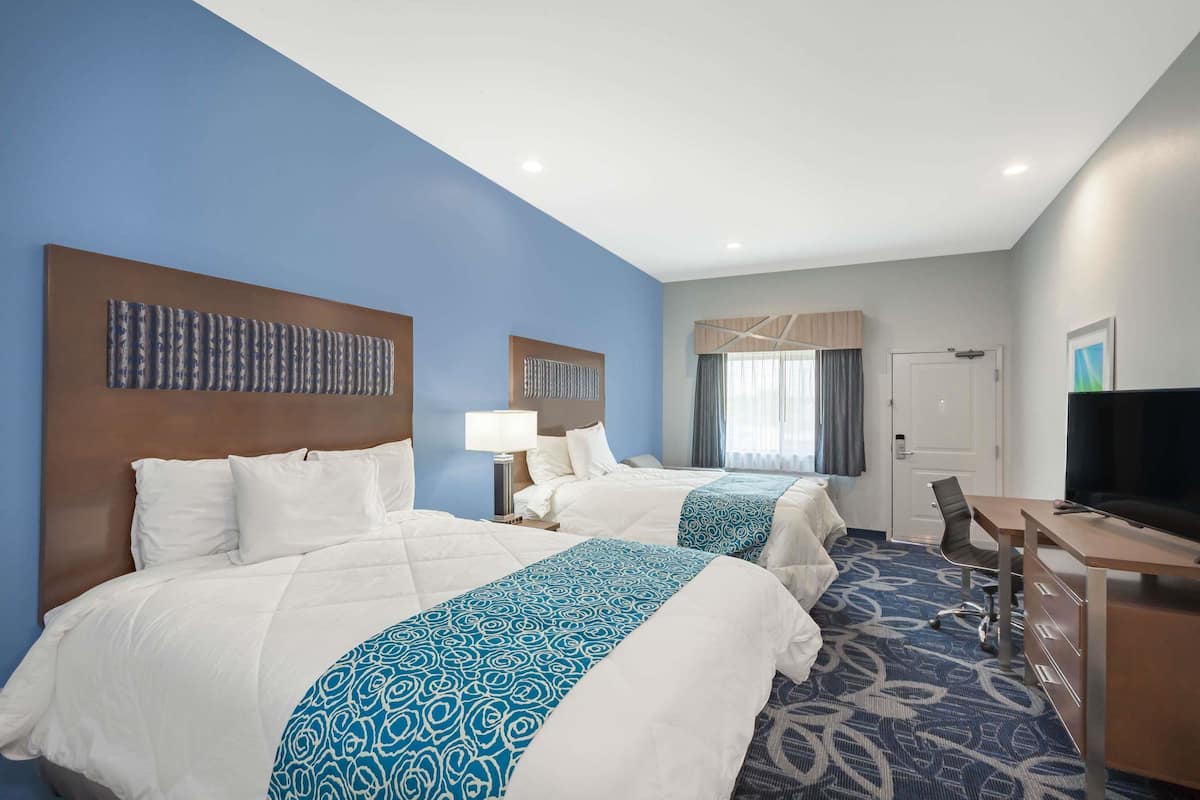 A hotel room with two beds, a desk, a TV, and a window with curtains.