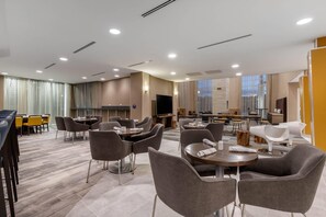 Um saguão de hotel com várias áreas de estar, uma televisão e uma grande janela.