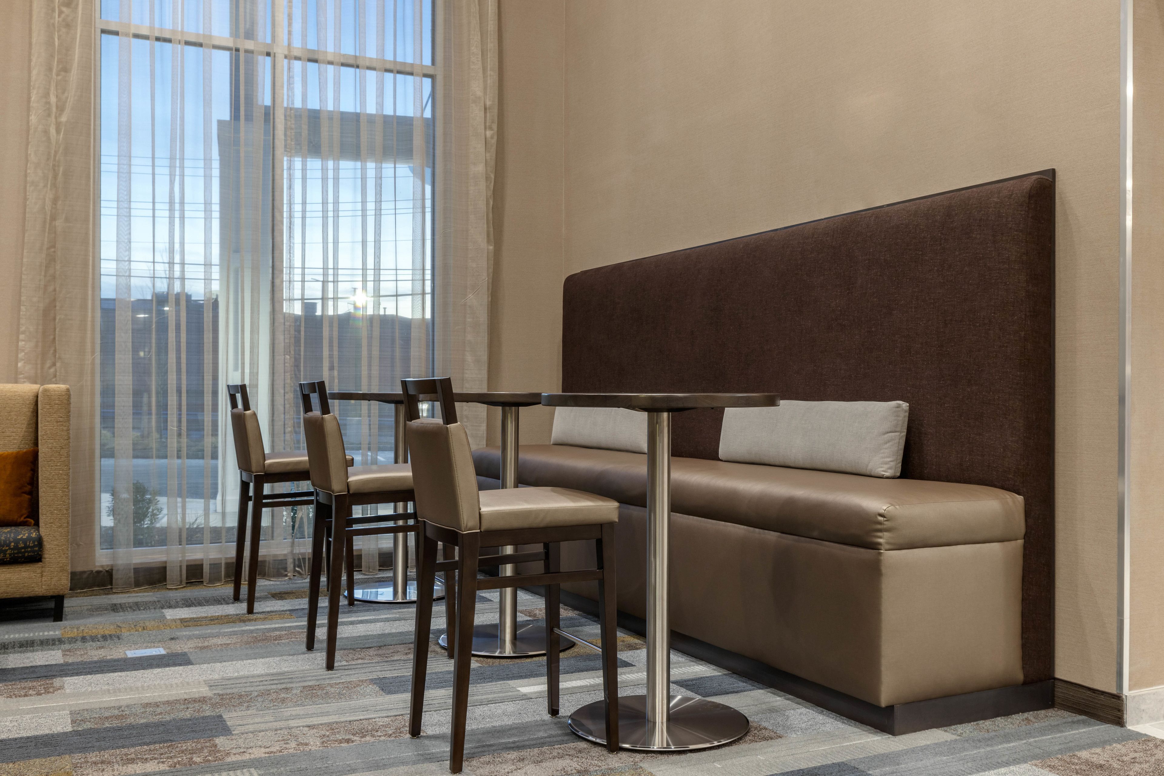 Habitación de hotel moderna con sofá, dos sillones, una mesita y un ventanal con cortinas translúcidas.