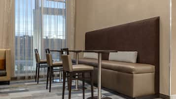Habitación de hotel moderna con sofá, dos sillones, una mesita y un ventanal con cortinas translúcidas.