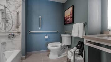 Une salle de bain avec des toilettes blanches, une barre d’appui, un porte-serviettes et un espace douche.