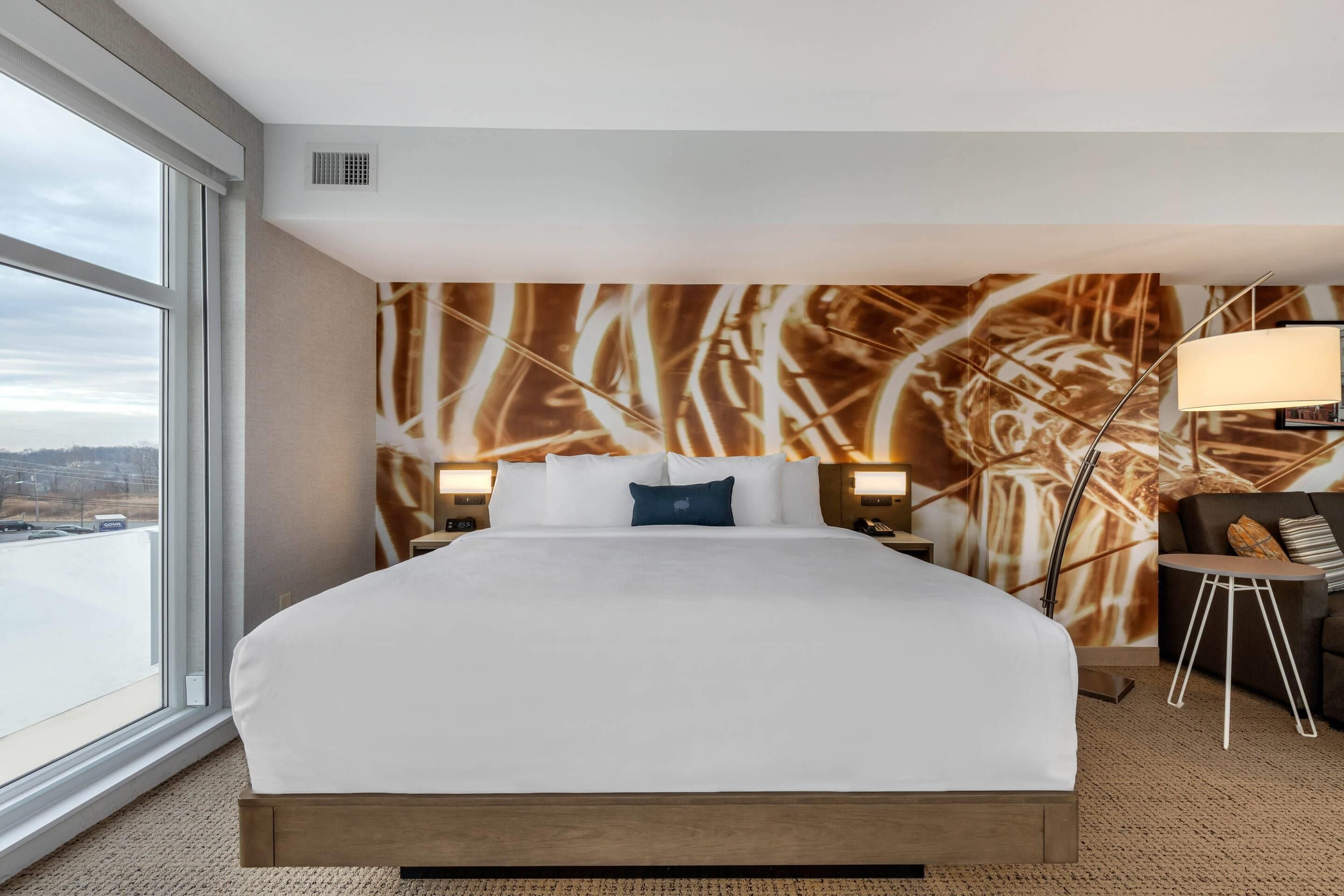 Ein Hotelzimmer mit einem großen Bett, einem Schreibtisch, einem Stuhl und Blick auf die Stadt durch das Fenster.