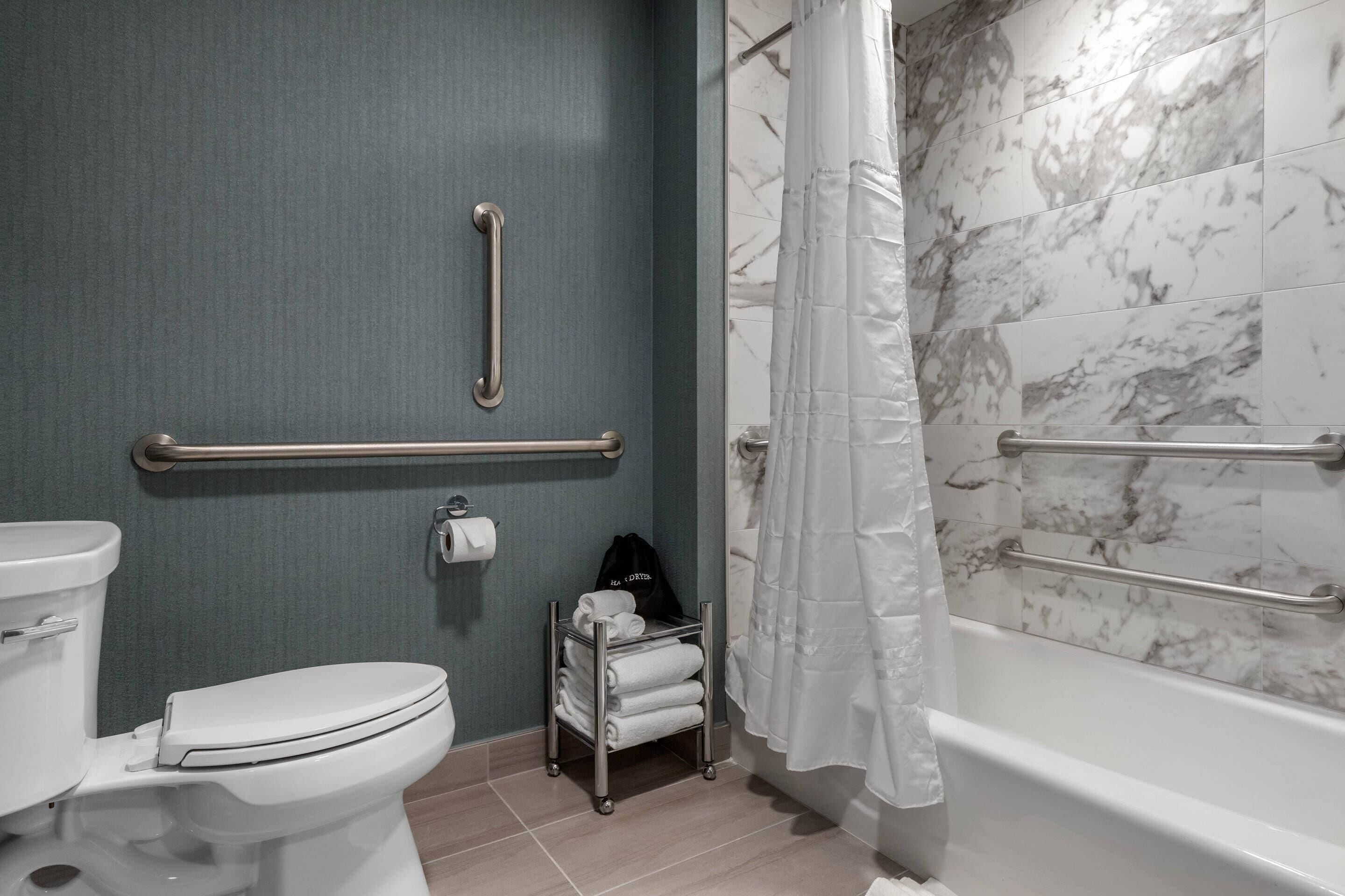 A bathroom with a toilet, a hand dryer, a towel rack, and a shower with a marble wall.
