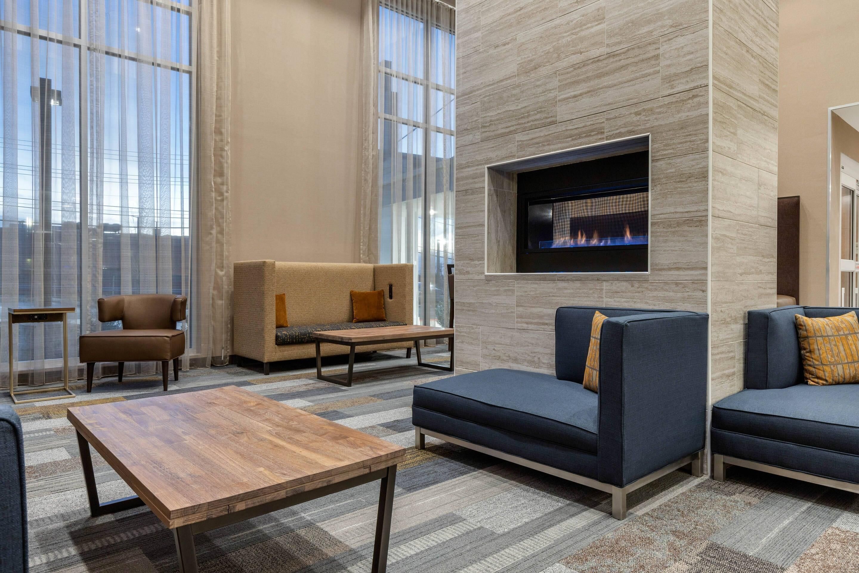 Un espace de détente moderne, doté de sièges confortables, d’une cheminée et de grandes fenêtres.