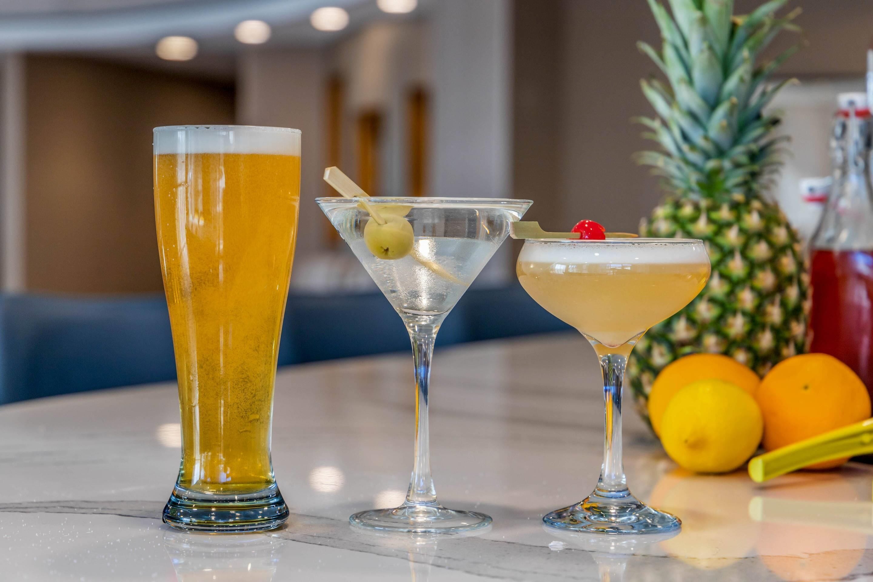 Tres tipos diferentes de bebidas sobre una barra, con frutas y una piña al fondo.