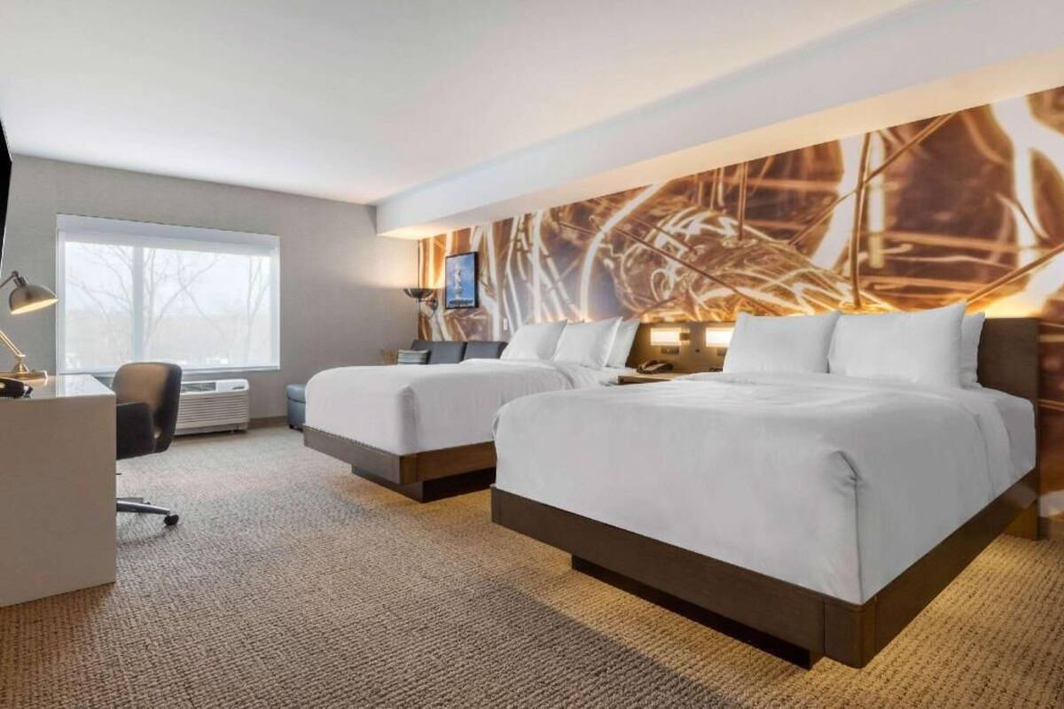 Hotellihuone, jossa on kaksi sänkyä, työpöytä, tuoli ja suuri, abstrakti seinämaalaus.