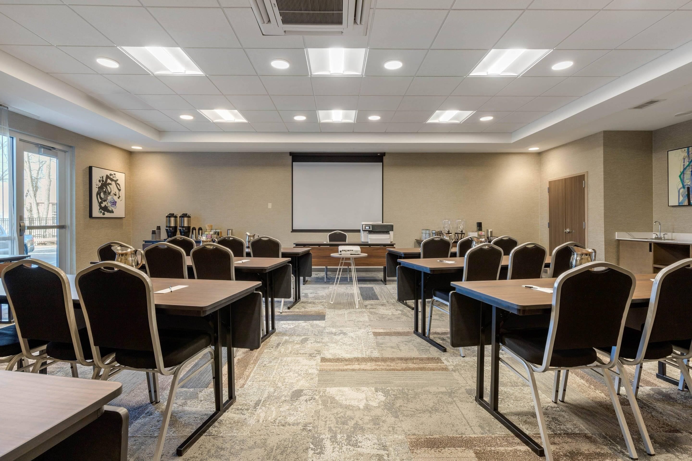 Un salón de conferencias con una pantalla de proyector, varias mesas y sillas.