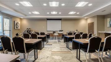 Un salón de conferencias con una pantalla de proyector, varias mesas y sillas.