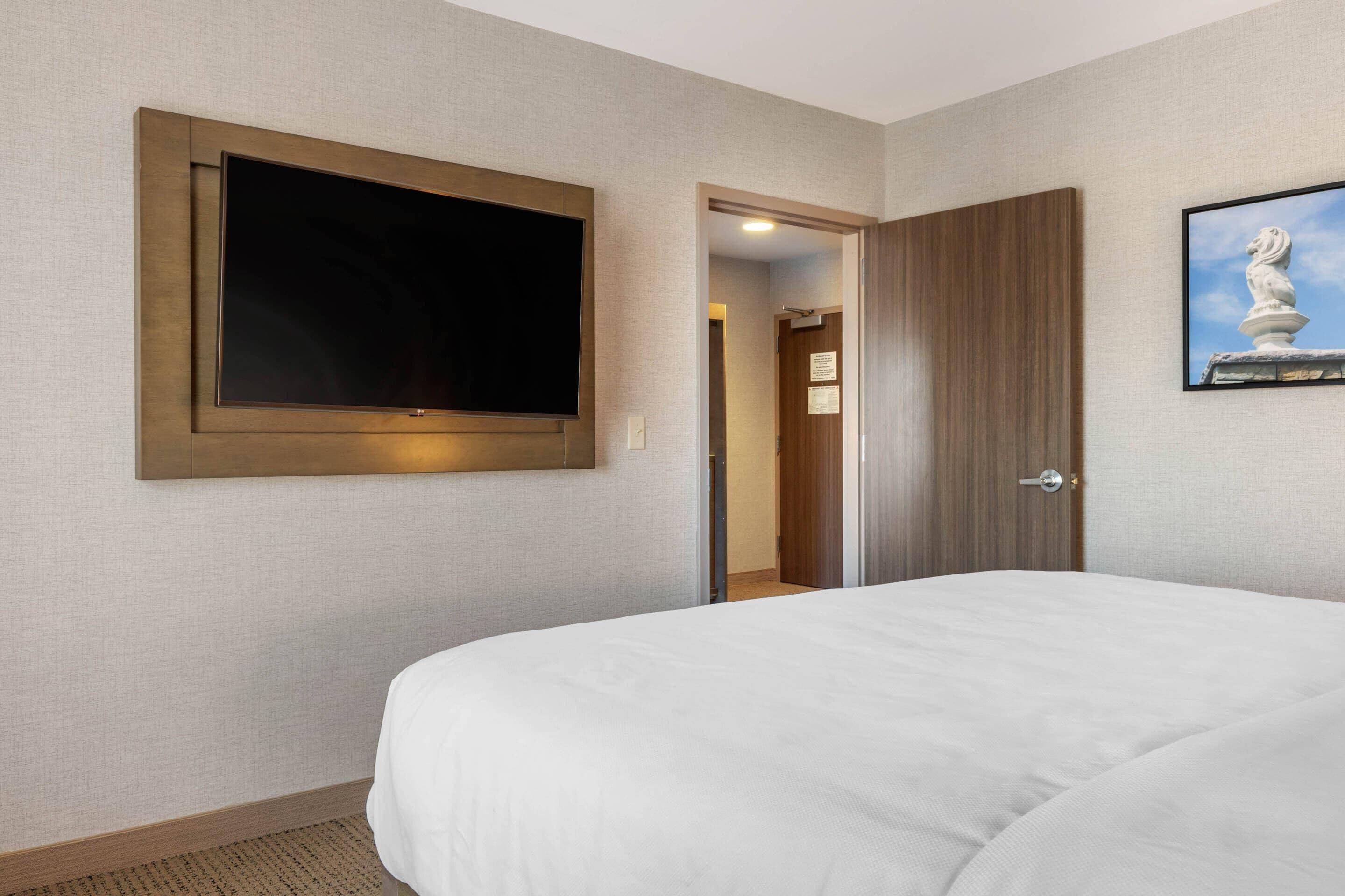 Et hotelværelse med en stor seng, et fladskærms-tv på væggen, en dør og en statue.