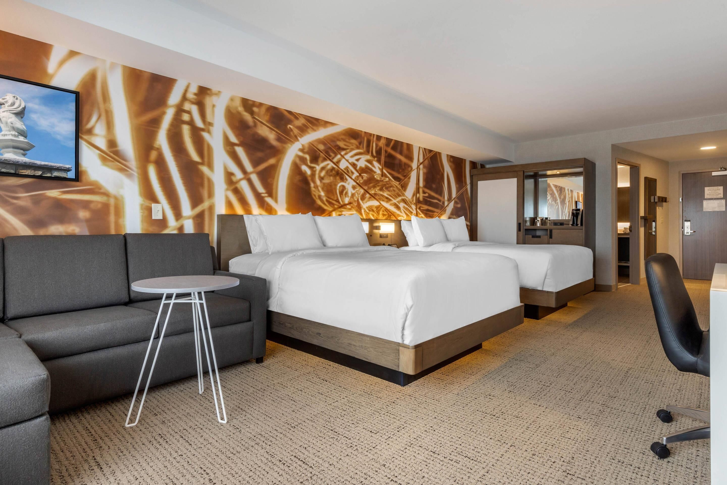 A hotel room with a double bed, a sofa, a small round table, and a wall-mounted TV.