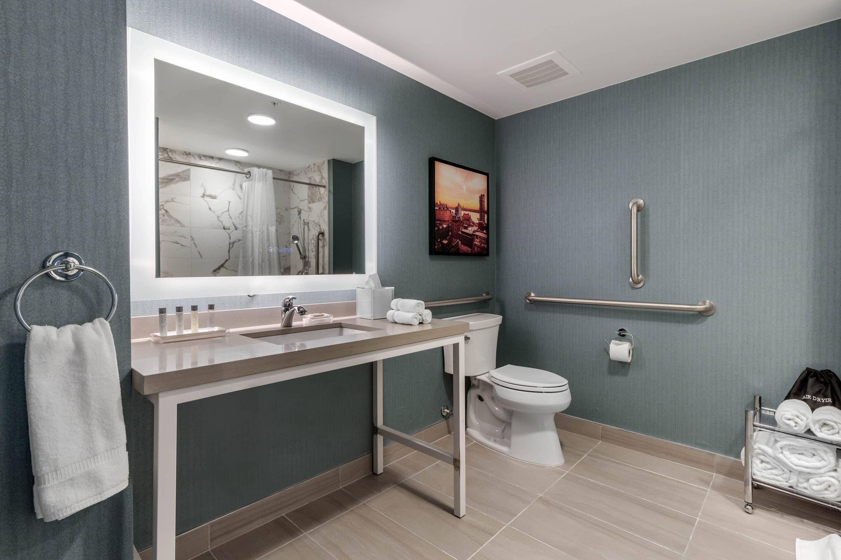 A modern bathroom with a marble vanity, a toilet, and a handrail for accessibility.