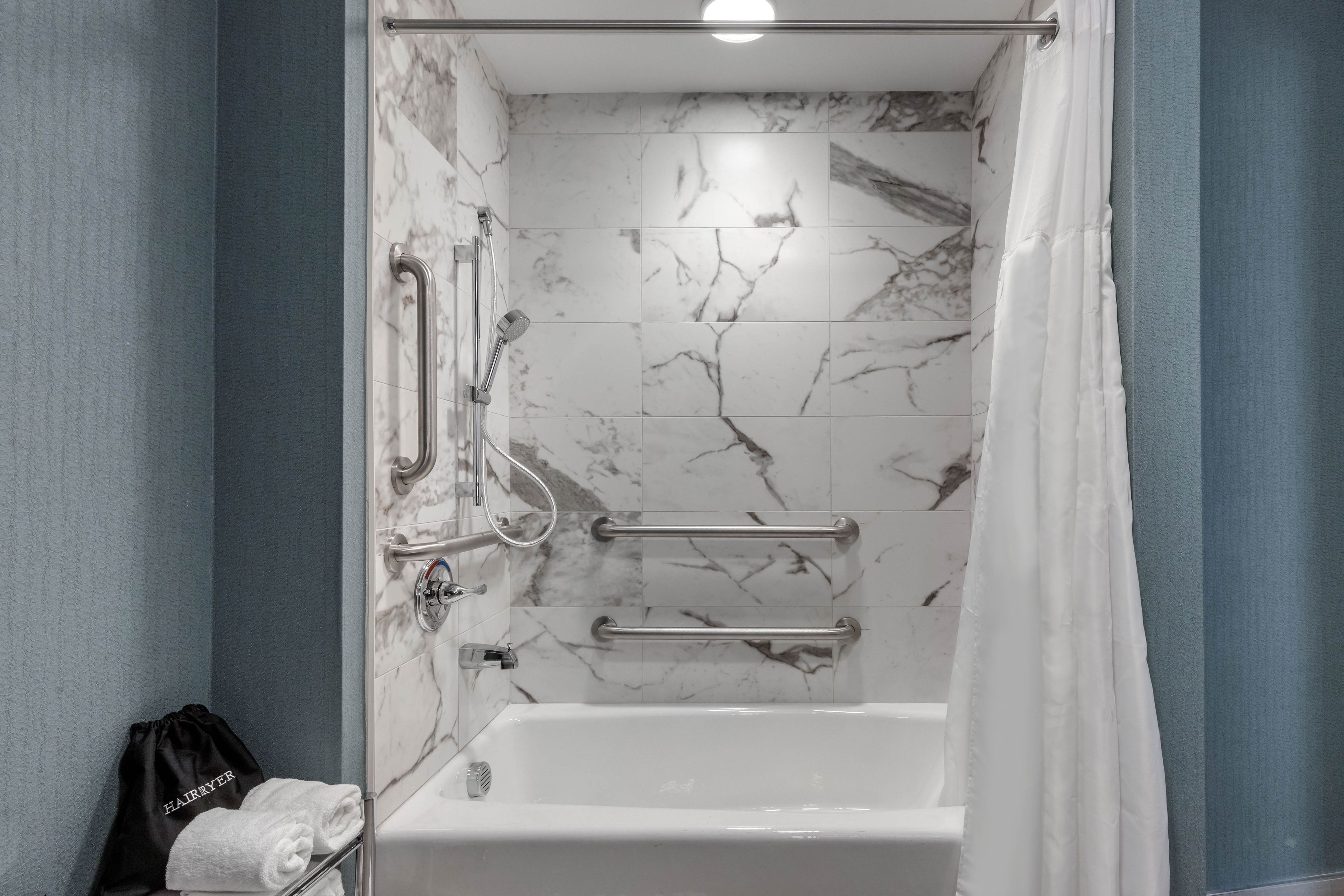 A bathroom with a shower, grab bars, and a towel rack.