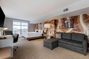 Quarto de hotel com cama, sofá, escrivaninha e uma janela grande.