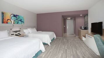 Habitación de hotel con dos camas, televisión, escritorio y un cuadro en la pared.