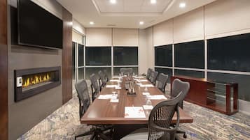 Una sala de conferencias con una mesa larga, sillas, un televisor de pantalla plana, chimenea y ventanas amplias.