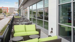 An outdoor seating area with wicker furniture and green cushions, large windows, and a view of the street.