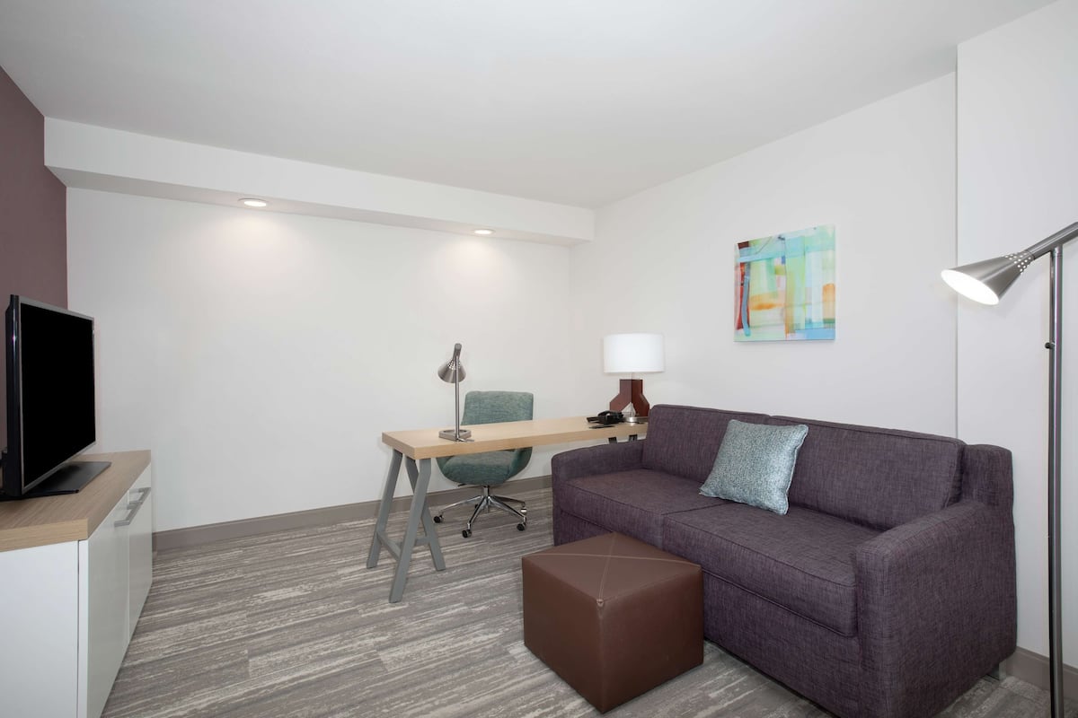 Una habitación moderna con sofá, escritorio, silla, televisor y lámpara.