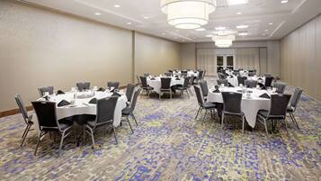 A conference room with multiple tables and chairs, arranged in rows, with a patterned carpet and a plain wall.