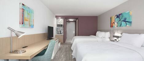 Une chambre d’hôtel équipée d’un bureau, de deux lits, d’une chaise, d’une télévision et d’œuvres d’art accrochées aux murs.